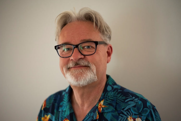 Portraifoto des Künstlers mit Brille und Bart und blauem Hemd
