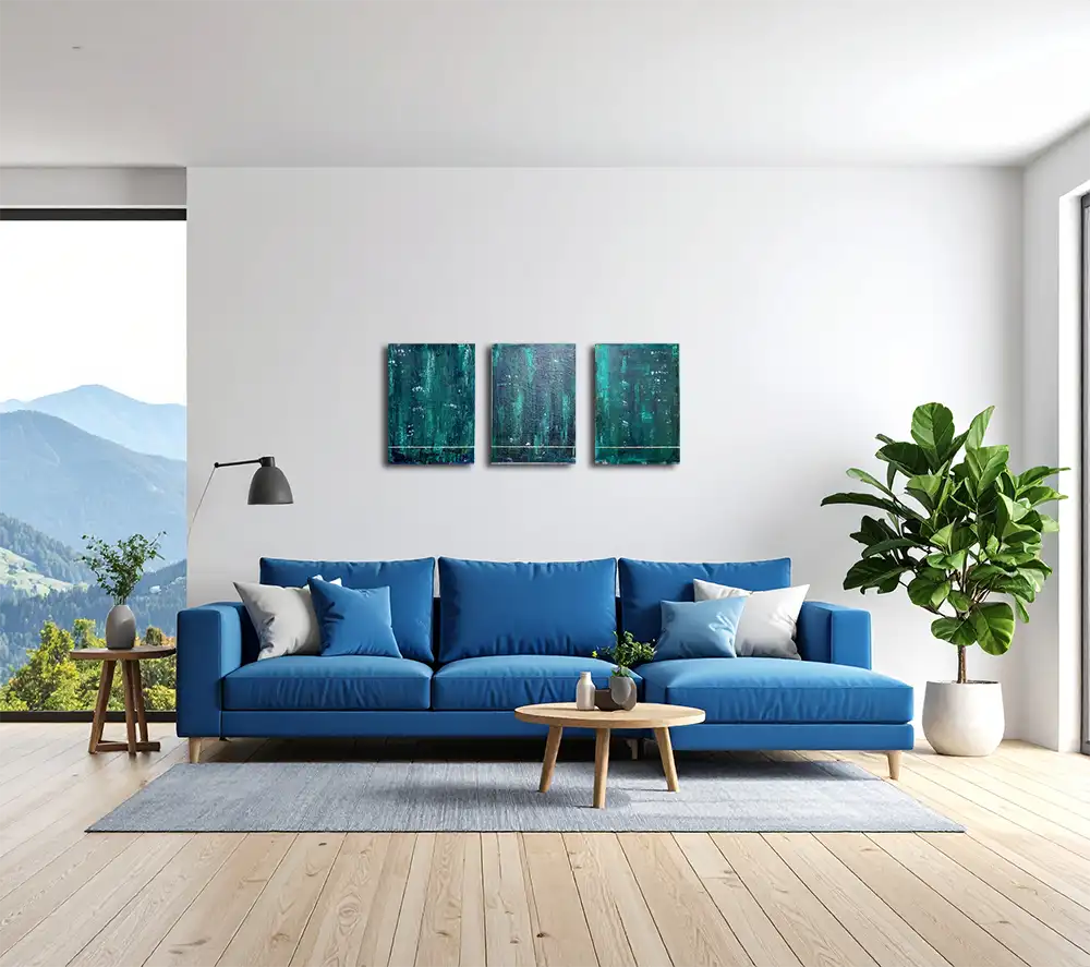 Drei Gemälde / Triptychon einer Serie in dunklem Grün an einer hellen Wand in einem modernen Wohnraum hängend, davor ein blaues Sofa
