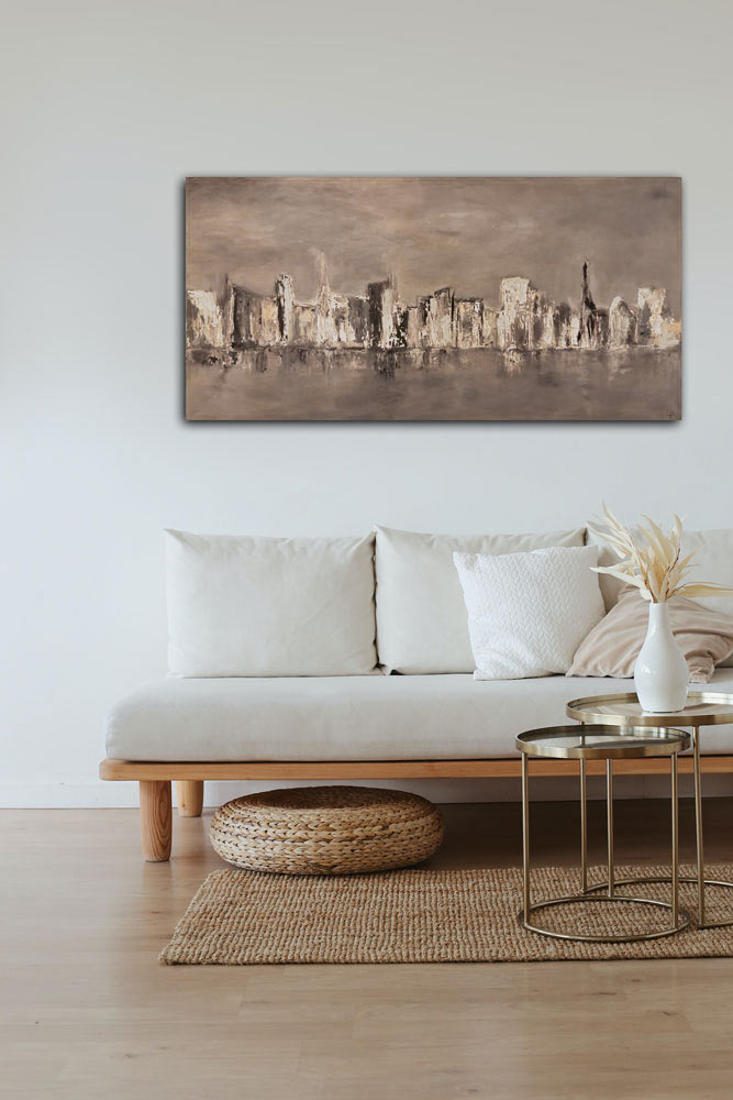 Das Bild city by the water hängt an einer weißen Wand, davor ein helles Sofa