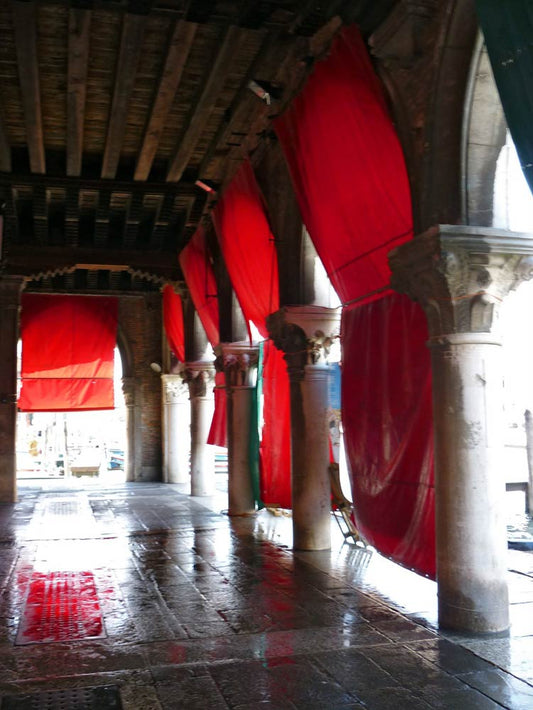 Ein Torgang in Venedig, Säulen und rote Tücher im Sonnenschein