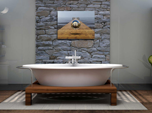 Eine Kugel schwebt über einem Steg der in die Ostsee führt-Surreales Werk, an einer Steinwand über eine  Badewanne hängend.