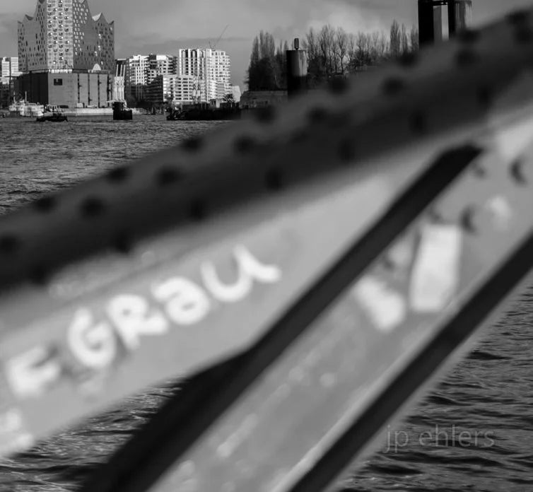 Ein schwarz Weiß Foto der Elbe mit Elbphilharmonie, Hanseatic Trade Center, Fähren und einem Brückenbogen, Detailansicht des Brückenbogens im Vordergrund
