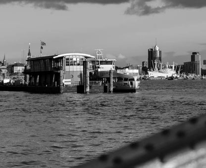 Ein schwarz Weiß Foto der Elbe mit Elbphilharmonie, Hanseatic Trade Center, Fähren und einem Brückenbogen, Detaiansicht der Gebäude auf der anderen Elbseite