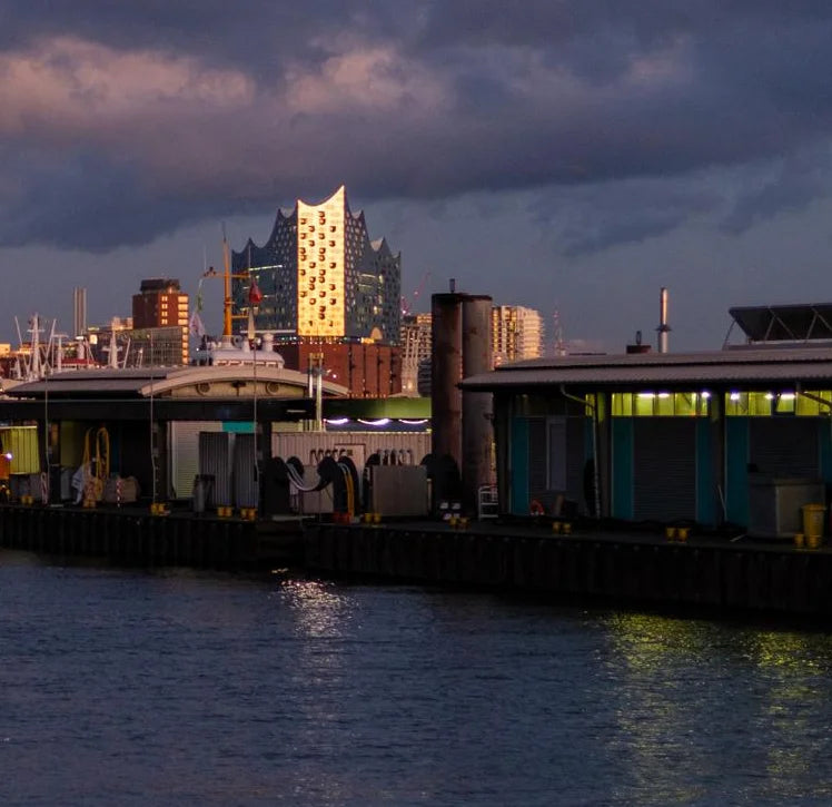 Farbfotografie des Hafens, das Abendlicht spiegelt sich in der Fassade der Elbphilharmonie, leichte Wolken am Himmel.