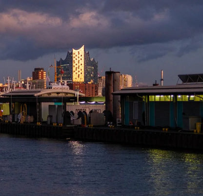 Farbfotografie des Hafens, das Abendlicht spiegelt sich in der Fassade der Elbphilharmonie, leichte Wolken am Himmel.