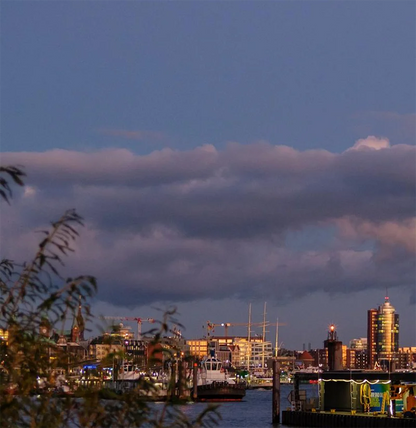 Farbfotografie des Hafens, das Abendlicht spiegelt sich in der Fassade der Elbphilharmonie, leichte Wolken am Himmel., Detailansicht mit Fähren