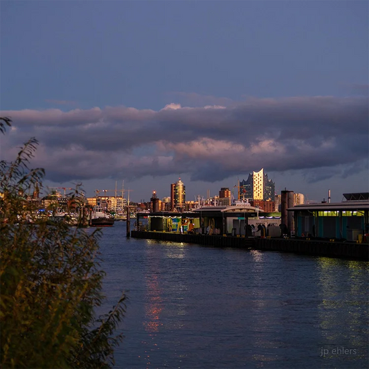 Farbfotografie des Hafens, das Abendlicht spiegelt sich in der Fassade der Elbphilharmonie, leichte Wolken am Himmel. Detailansicht mit Elbphilharmonie
