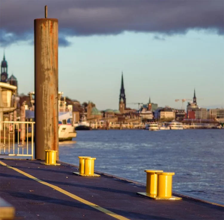 Das Farbfoto von J.P. Ehlers zeigt ein mildes Licht, die Elbe, einen Anleger, ein urbanes Fotos, Detailansicht mit gelben Pollern
