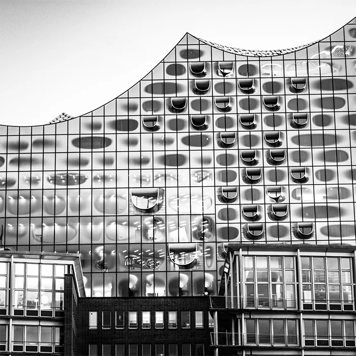 Schwarz-weiß Foto der Elbphilharmonie, mit anderem Gebäude im Vordergrund