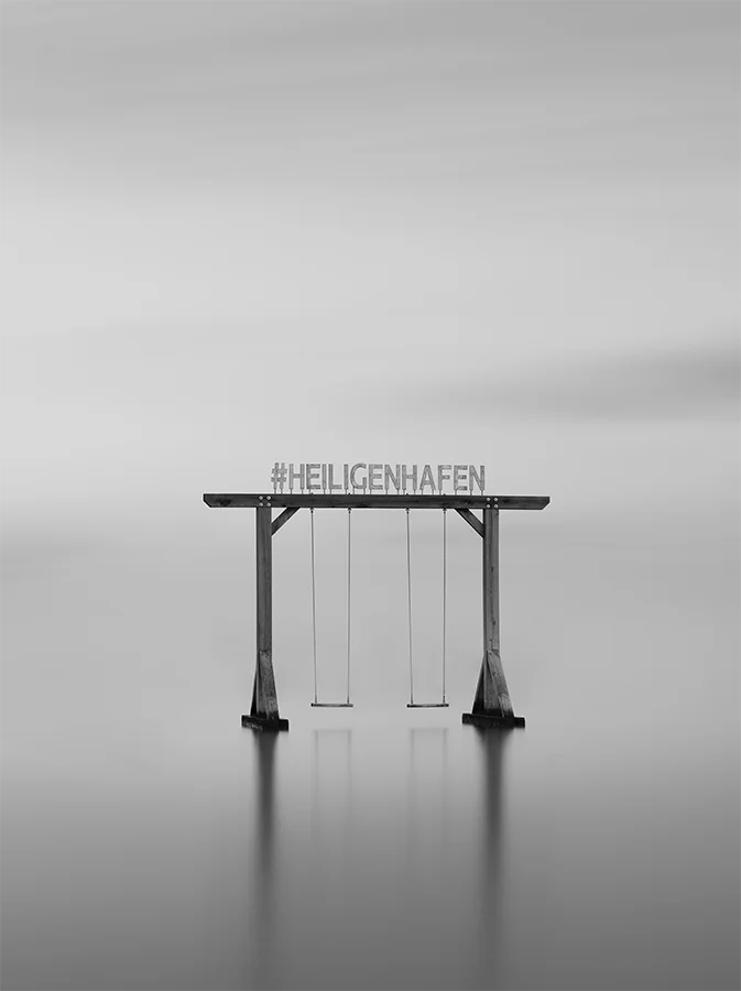 Der Schriftzug Heiligenhafen auf einer Schaukel im Wasser, s/w Langzeitbelichtung