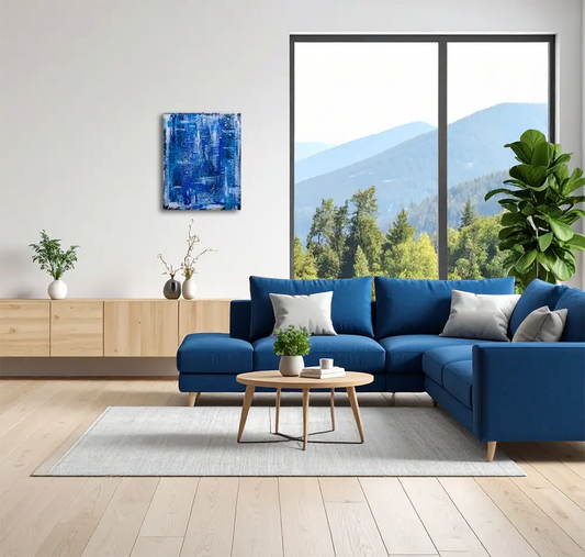 Abstraktes Gemälde, Hochformat, mit blauen und weißen Strukturen erinnert an die Meeresoberfläche im Sturm. An einer Wand hängend in einem modernen Wohnraum mti blauem Sofa.