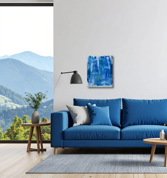 Abstraktes Gemälde, Hochformat, mit blauen und weißen Strukturen erinnert an die Meeresoberfläche, An heller Wand hängend in modernem Wohnzimmer mit großem blauen Sofa und links Fenster.