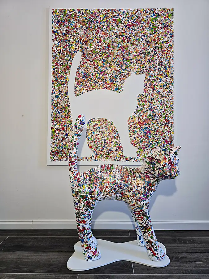 Eine bunte Katze steht vor einer bunten Leinwand mit den Umrissen  der Katze.