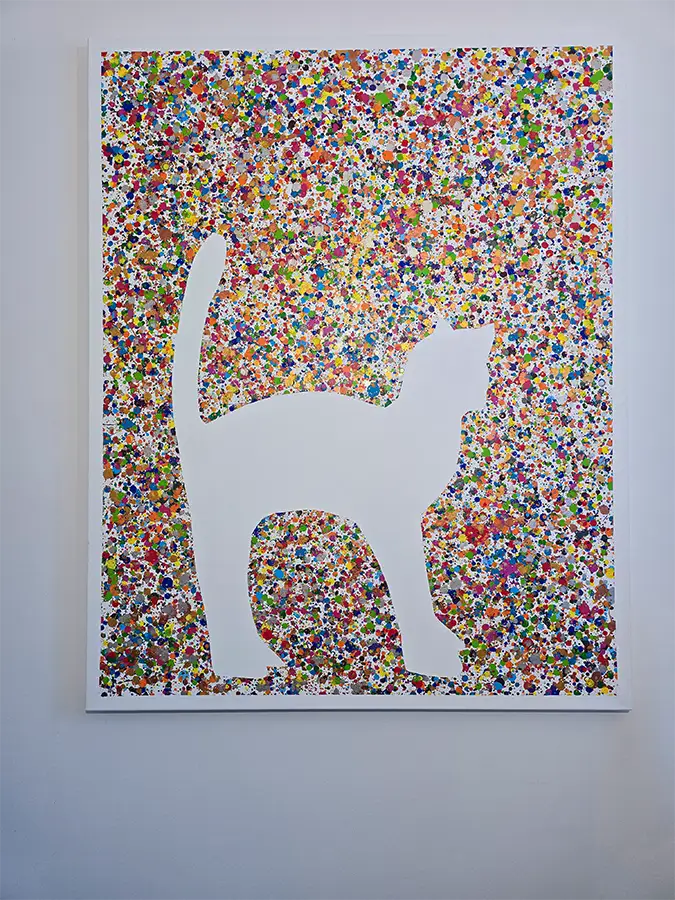 Eine bunte Katze steht vor einer bunten Leinwand mit den Umrissen  der Katze, Details des  Gemäldes