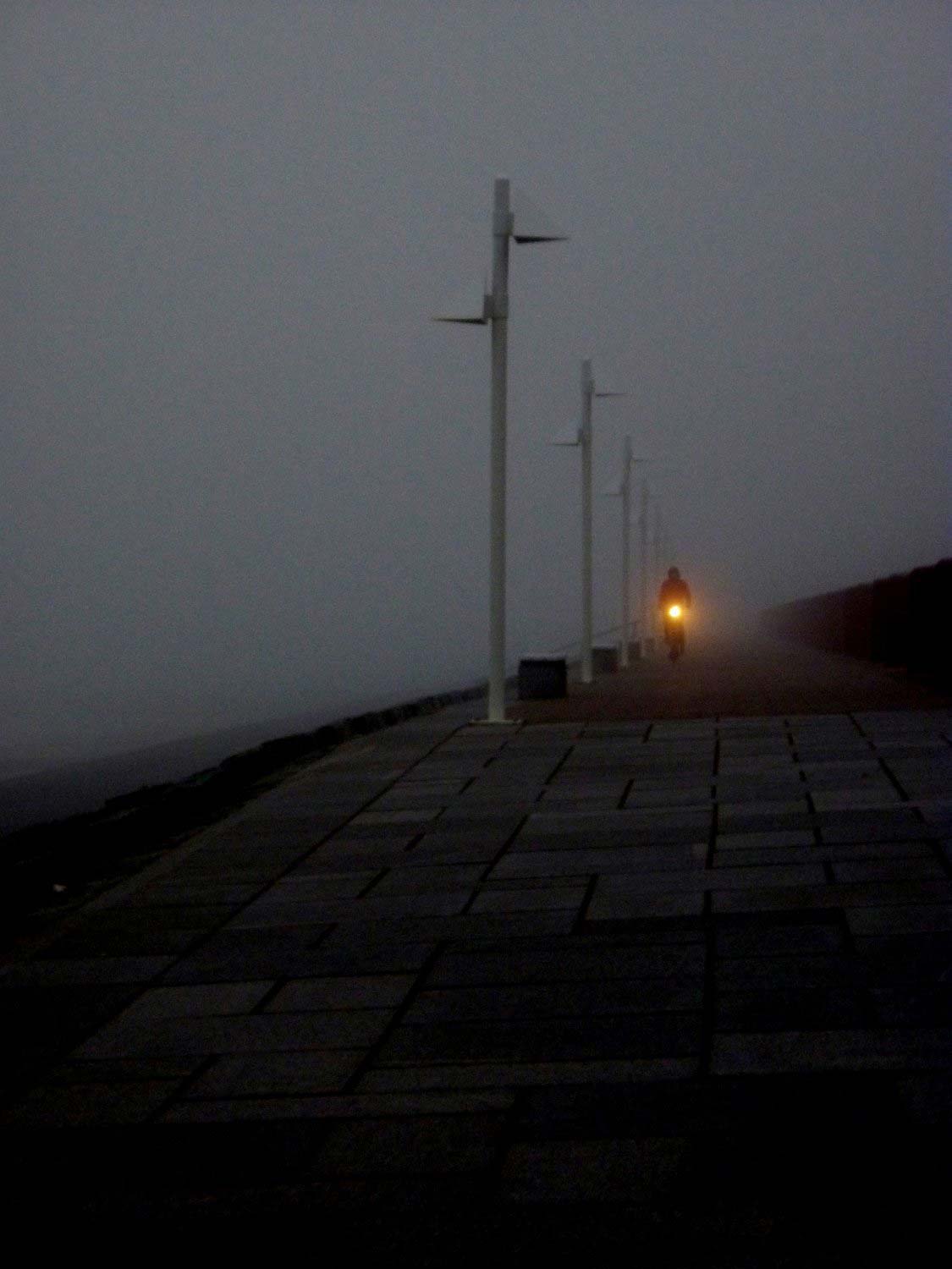 ein Radfahrer fährt in der Dunkelheit auf dem Deich, die Lampe des Rades leuchtet