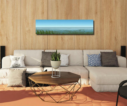 Panoramafoto des Watts vor Sylt, eine Möve ist zu sehen, weiter Horizont mit Nordsee, an Holzwand hängend mit hellem Sofa